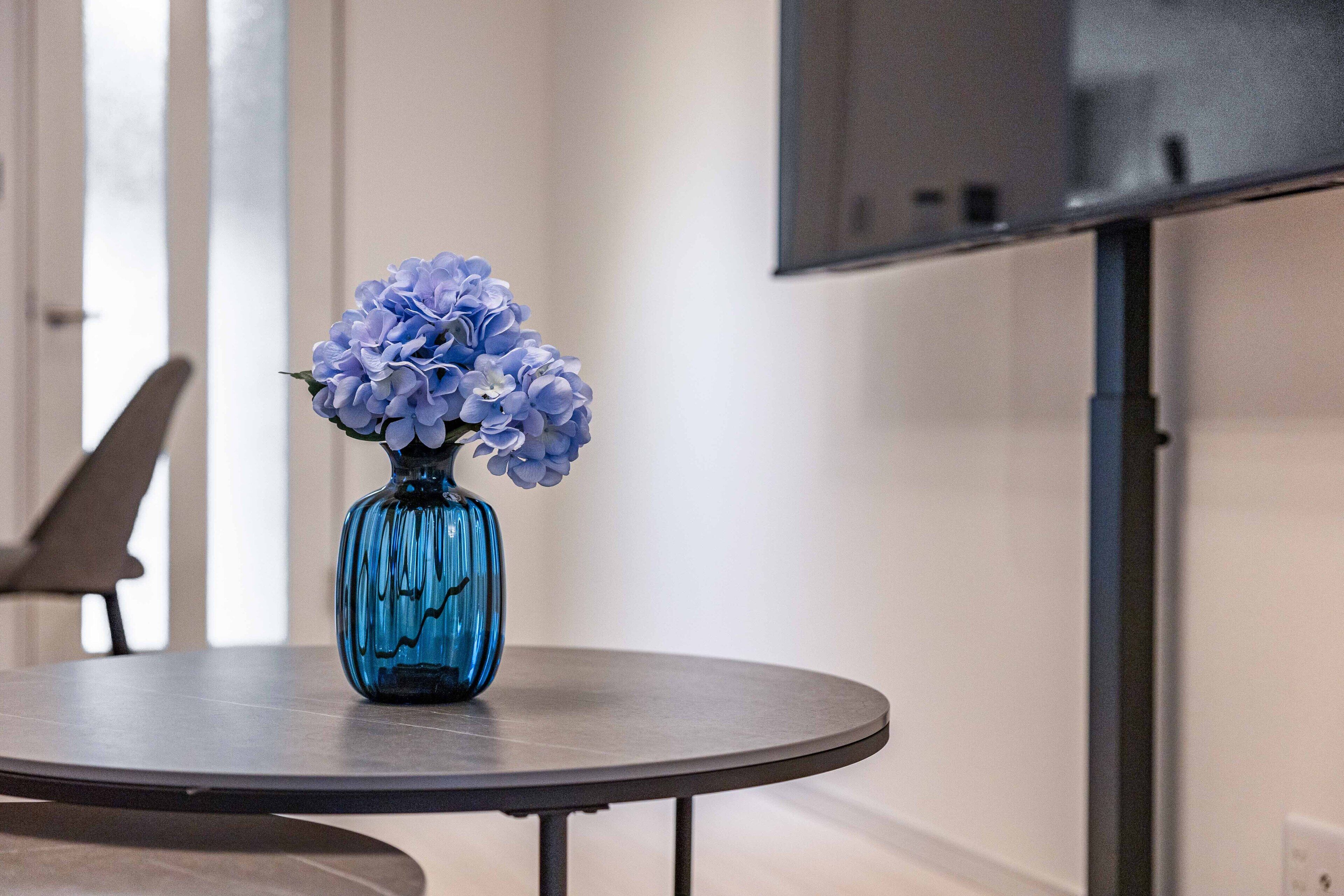 A blue vase with flowers on a round table.