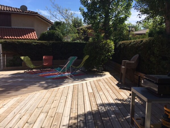 Een houten terras met lounge fauteuils, een barbecue en een houten bank.