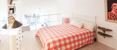 A bedroom with a checkered bedspread, a white headboard, a bedside table, and a hanging lamp.