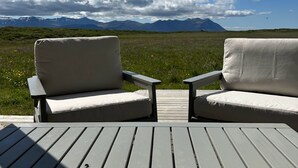 Una terraza con dos sillas frente a un paisaje montañoso bajo un cielo parcialmente nublado.