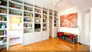 A spacious room with wooden flooring, white built-in bookshelves, a black leather sofa with red cushions, a floor lamp, and a large abstract painting on the wall. - Carlo's welcome in Trastevere (Roma)