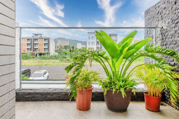 Un balcon agrémenté de plantes en pot, d’où l’on peut admirer des immeubles et un parking.