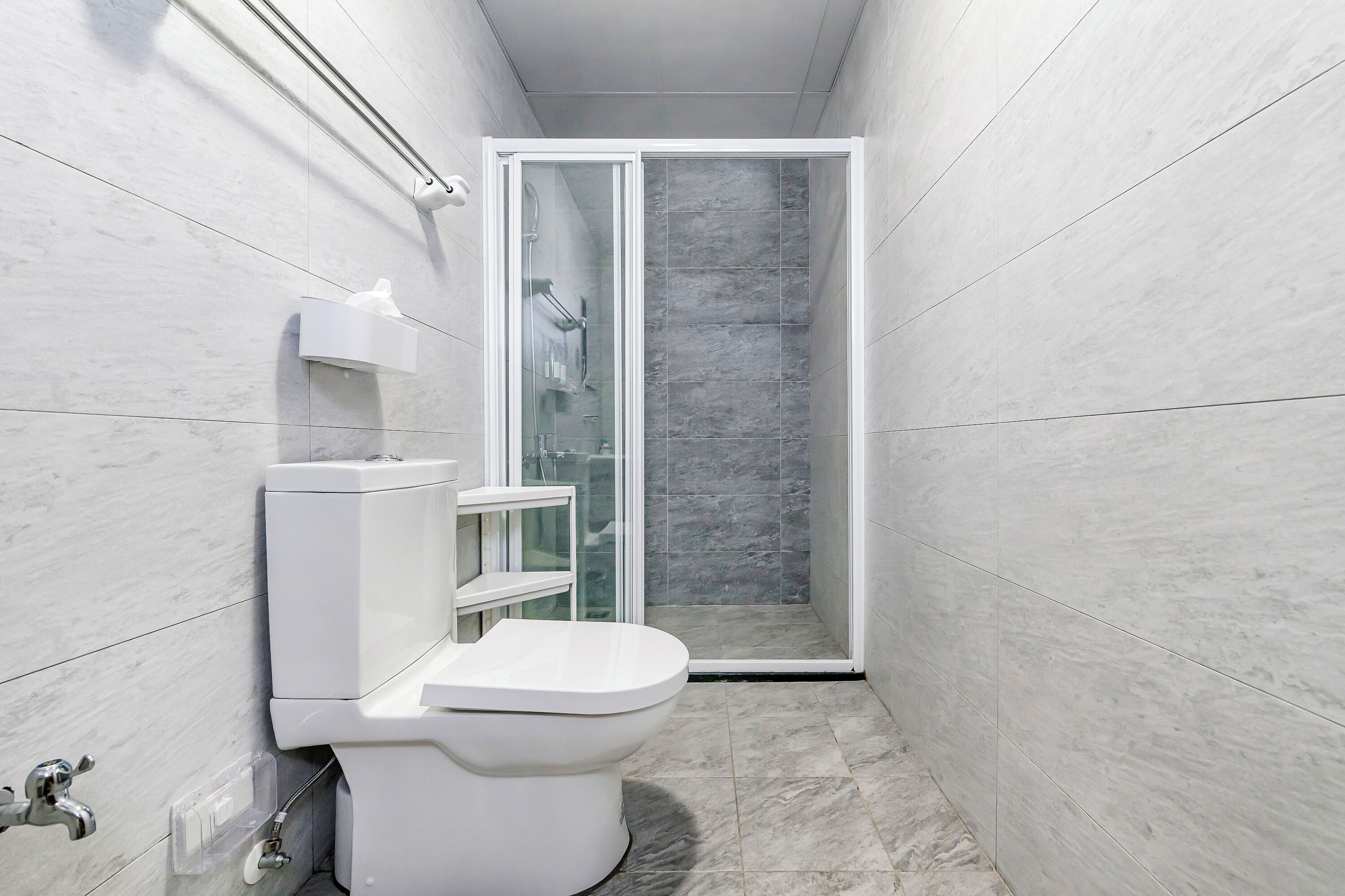 A modern bathroom with a toilet, a glass shower enclosure, and a marble-tiled floor.