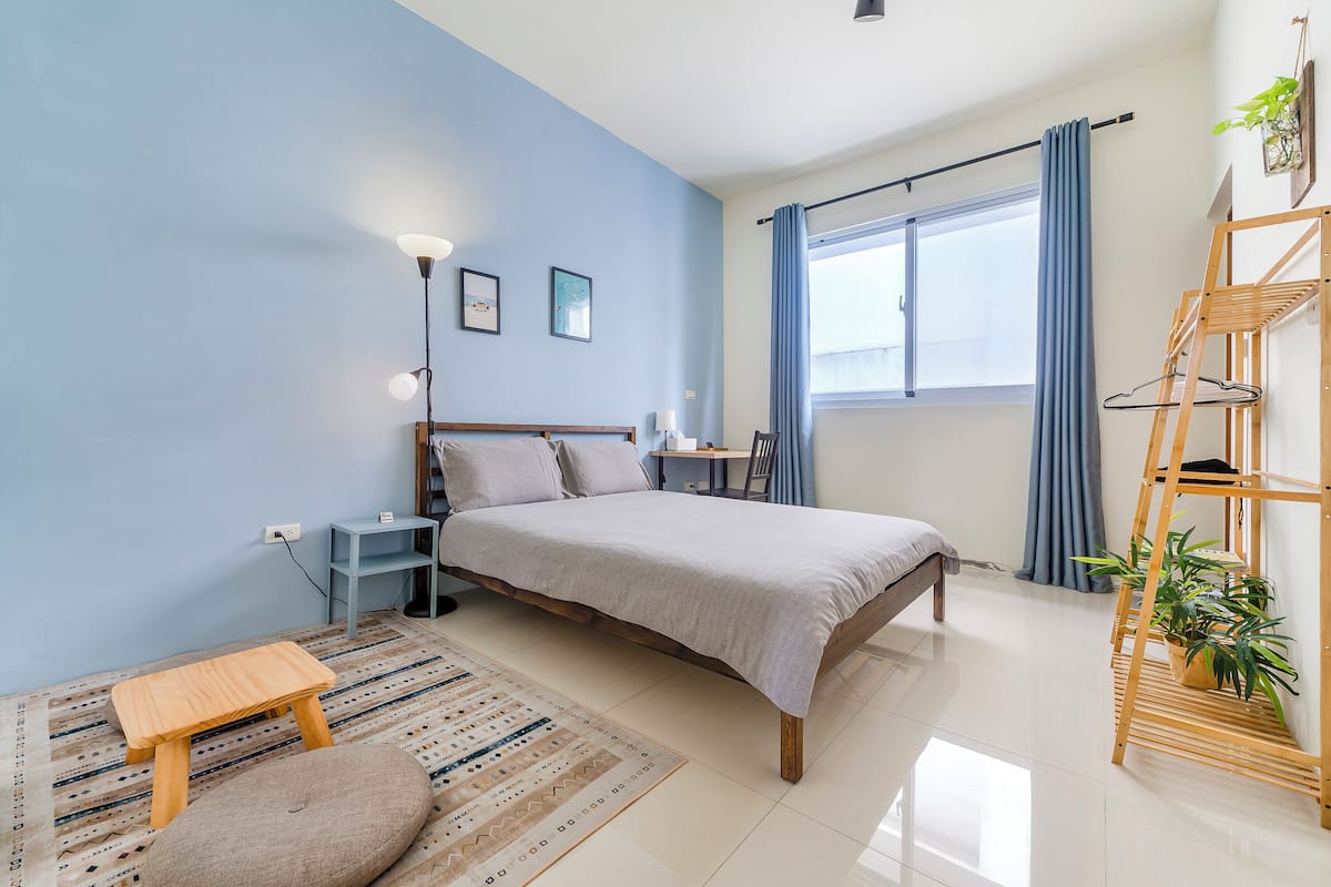 A bedroom with a bed, bedside table, lamp, and a small wooden stool.