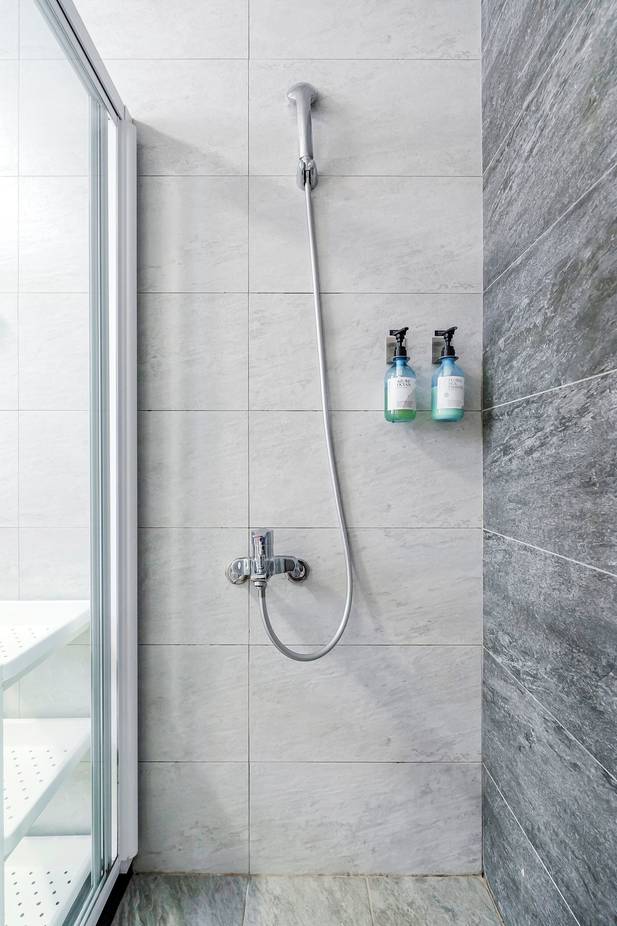 Eine Dusche mit Duschbrause und zwei Flaschen Shampoo und Conditioner an der Wand.