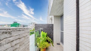 A balcony with a potted plant, a glass railing, and a view of the cityscape. - Stay in Jialeshuei (Hengchun)