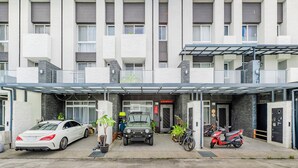 A modern building with a covered entrance, a white car, a motorcycle, and a green SUV parked in front. - Stay in Jialeshuei (Hengchun)