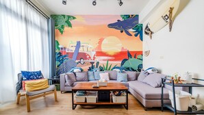 A living room with a sofa, a coffee table, and a mural of a beach scene. - Stay in Jialeshuei (Hengchun)