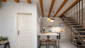 Una cocina moderna con una puerta blanca, vigas de madera, una escalera con barandilla metálica y una lámpara colgante.