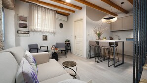 Una sala moderna con sofá, sillas, una mesita y una cocina que incluye una mesa de comedor y taburetes de bar.