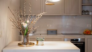 Una cocina moderna con encimera blanca, un florero con ramas y flores, y una pequeña planta en maceta.