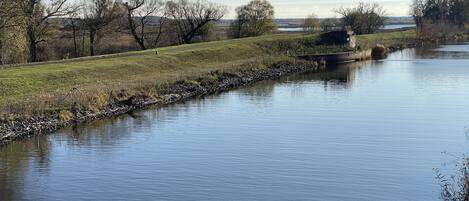 A calm river with a stone embankment, grassy banks, and trees in the background.
