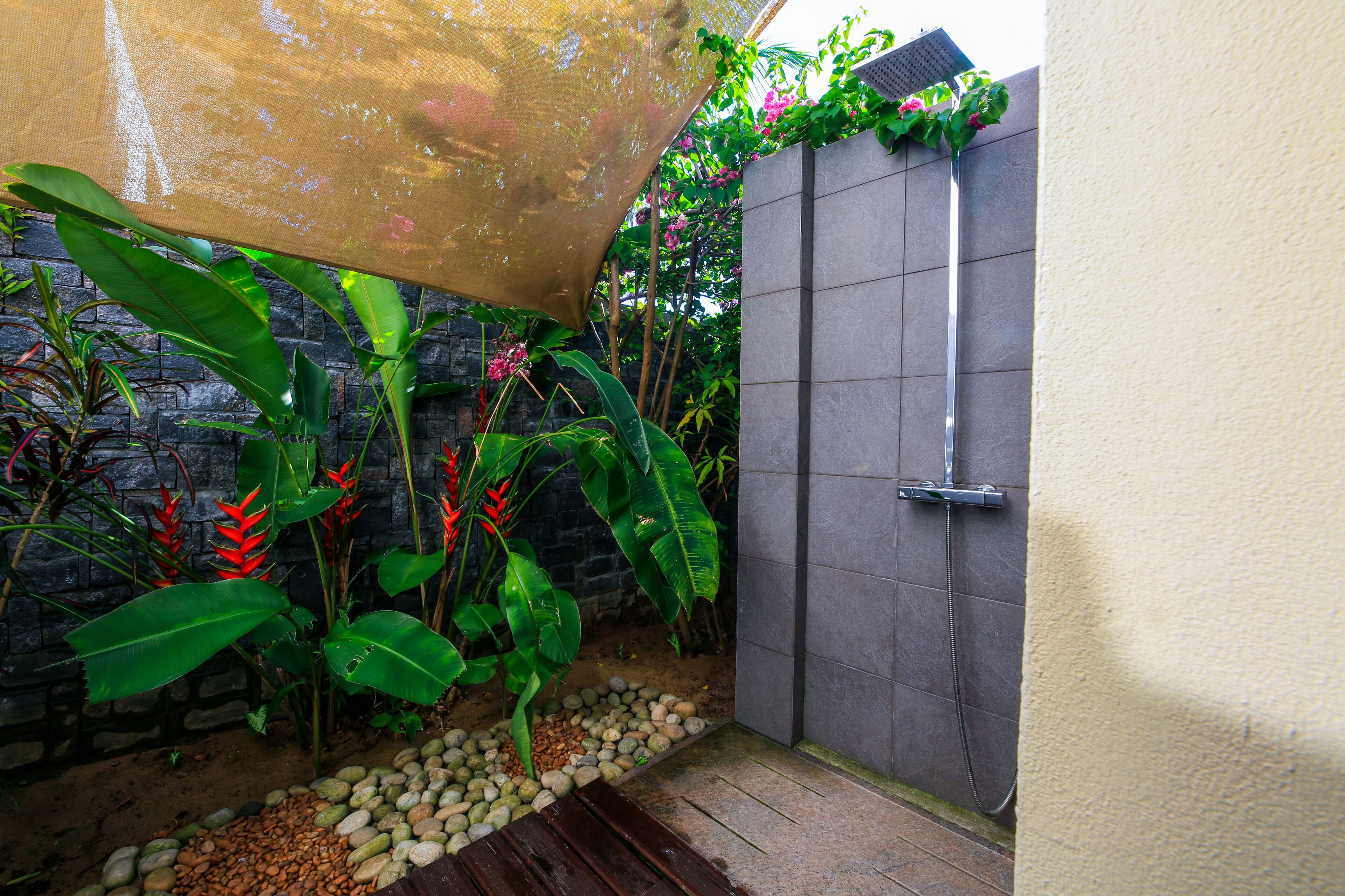 A private garden with a shower area, surrounded by tropical plants and a stone wall.