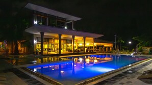 A modern hotel with a swimming pool, outdoor seating, and a well-lit facade. - Azura Golf Resort & Spa (Mahavelona)