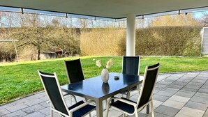 An outdoor patio with a rectangular table and four chairs, surrounded by a paved area and a grassy lawn. - Stilvolles Designappaetment mit Terrasse & Garten im Idylischem Bindlach (Bindlach)