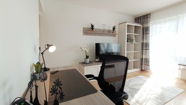 Una sala de estar moderna con un escritorio de madera, una silla de oficina negra, un televisor y una estantería.