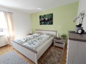 A bedroom with a bed, bedside tables, a nightstand, a wall-mounted clock, a potted plant, and a painting. - 80 qm Moderne Wohnung mit Balkon und Garten im Herzen von Tirschenreuth (Tirschenreuth)