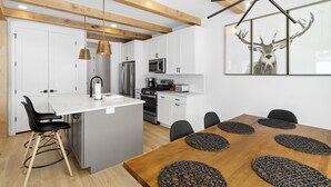 A modern kitchen with white cabinets, stainless steel appliances, and a wooden dining table with black chairs.