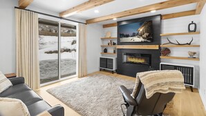 A modern living room with a fireplace, wooden beams, a sofa, and a sliding glass door to a snowy landscape.