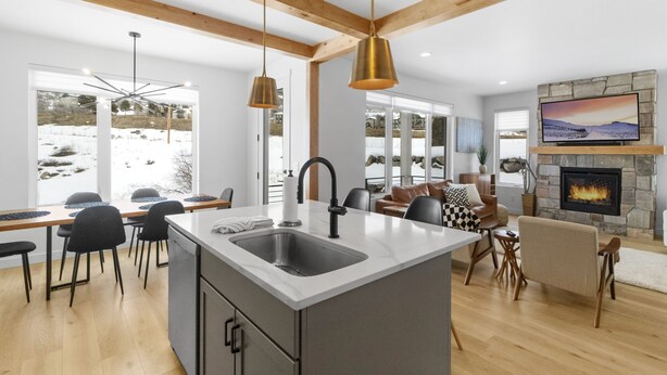 A modern kitchen with a central island, wooden beams, pendant lighting, and a stone fireplace.