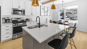 A modern kitchen with white cabinets, a central island, stainless steel appliances, and pendant lighting.
