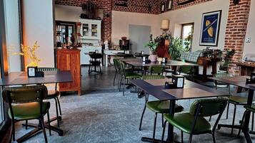 A spacious dining area with high ceilings and exposed brick walls, featuring multiple tables and chairs.