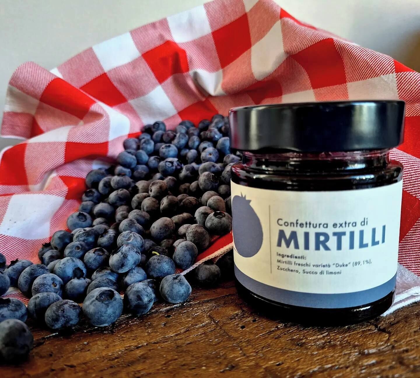 Un barattolo di confettura extra ai mirtilli, con mirtilli sullo sfondo.