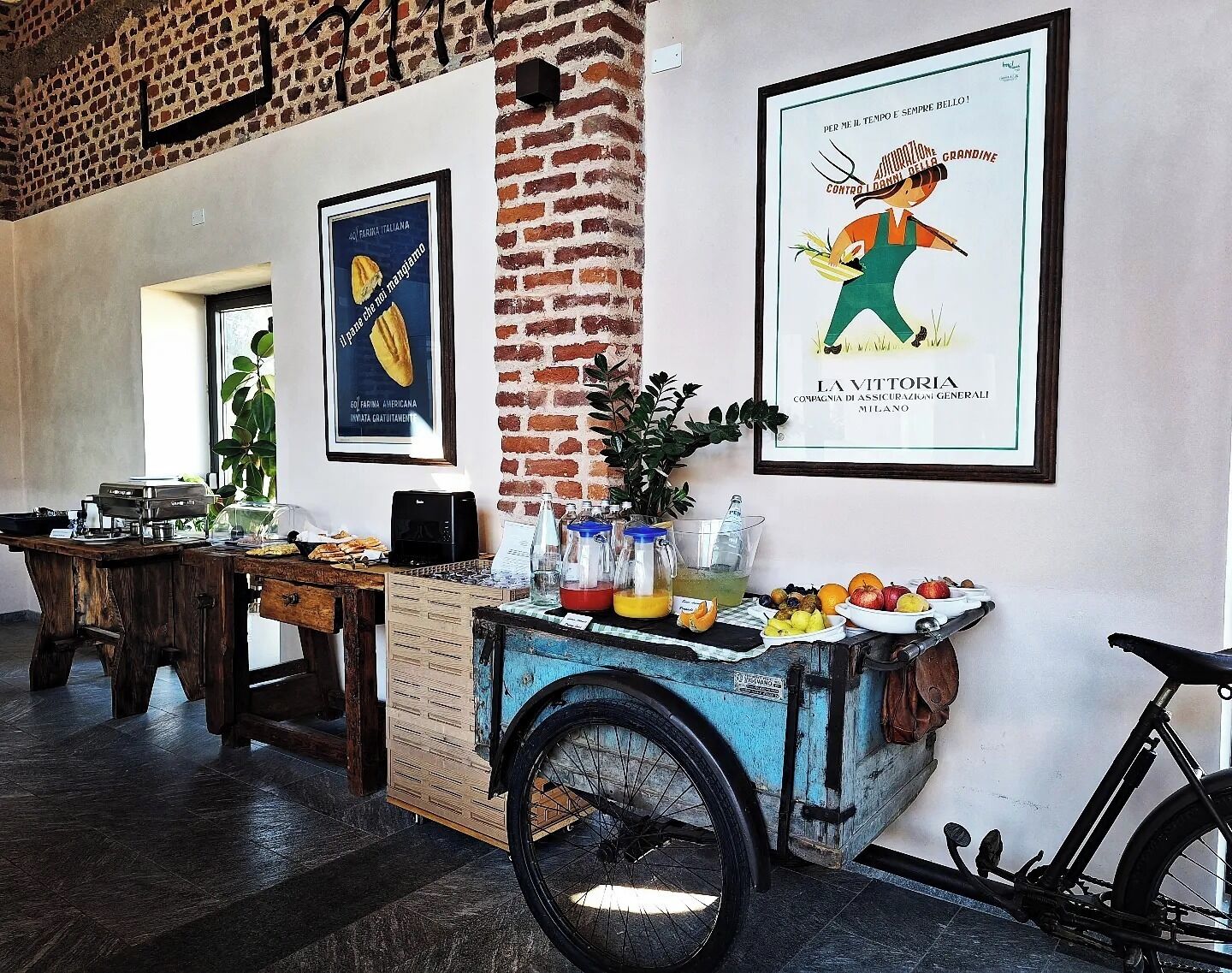 A room with a brick wall, a vintage cart with fruits and drinks, and a bicycle.