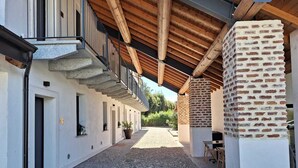 A covered outdoor corridor with a gravel path, wooden beams, and a brick column. - Cascina Mora Bassa (Vigevano)