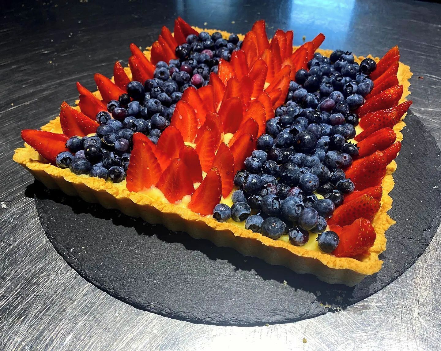 Een taart met aardbeien en bosbessen op een zwart leistenen bord.