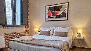 A neatly made bed with a white headboard, two bedside lamps, and a framed abstract painting above it. - Cascina Mora Bassa (Vigevano)