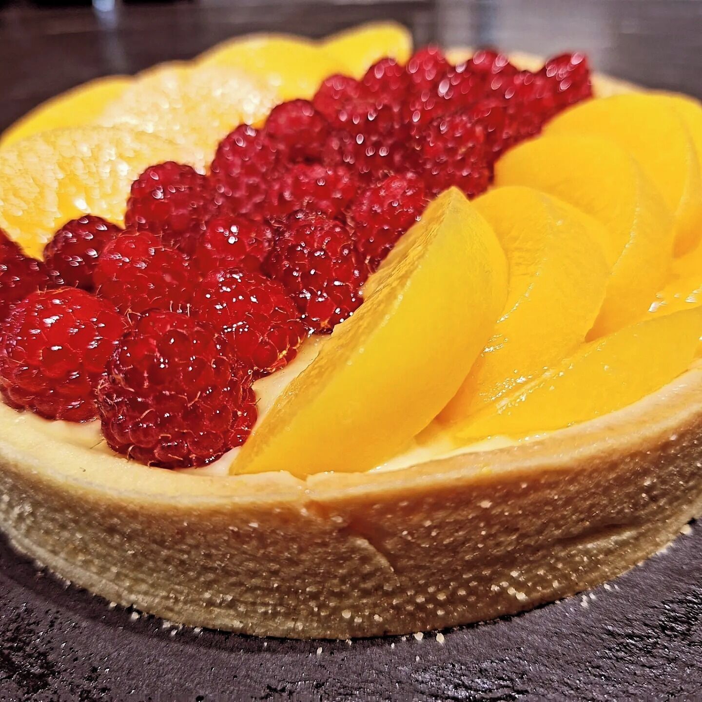 A dessert with a crust, topped with raspberries and peach slices.