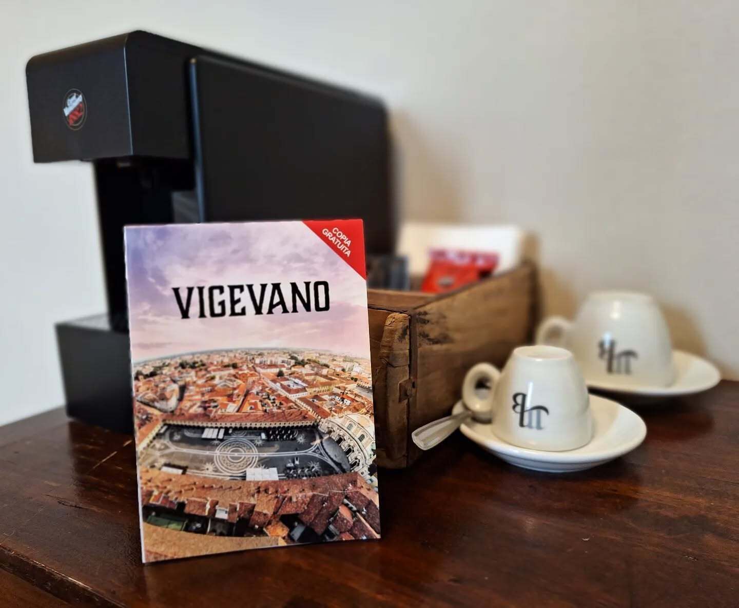 Un libro con el título "VIGEVANO" sobre una mesa junto a una cafetera y dos tazas.