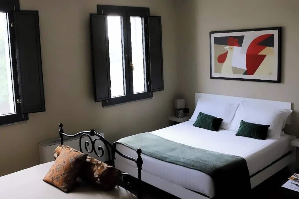 A bedroom with a bed, bedside table, lamp, and a window with shutters.