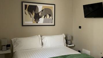 Een slaapkamer met een bed, een groene plaid, een lijst met een abstract schilderij, een flatscreen televisie en nachtkastjes met lampen.