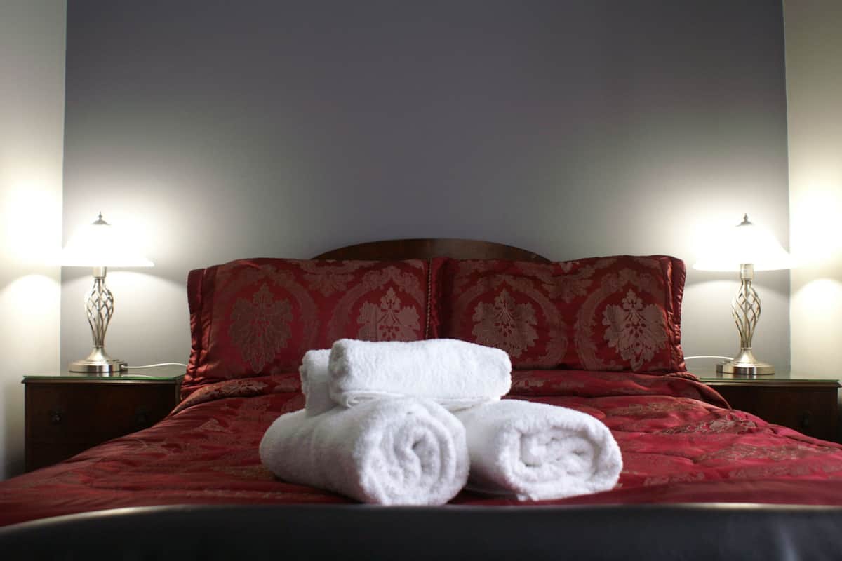 A neatly made bed with red bedding and white towels, two bedside lamps, and a wooden nightstand.