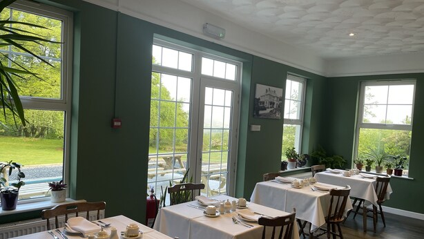 A dining area with tables set for service, large windows with views of greenery, and a ceiling with a textured design. - Moorlands (Barnstaple)