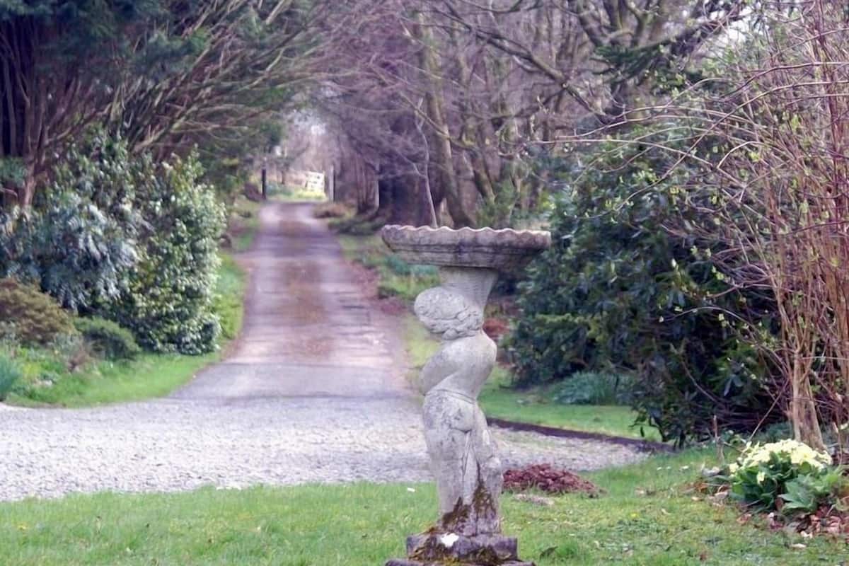 A garden pathway leading to a stone fountain with a statue base.
