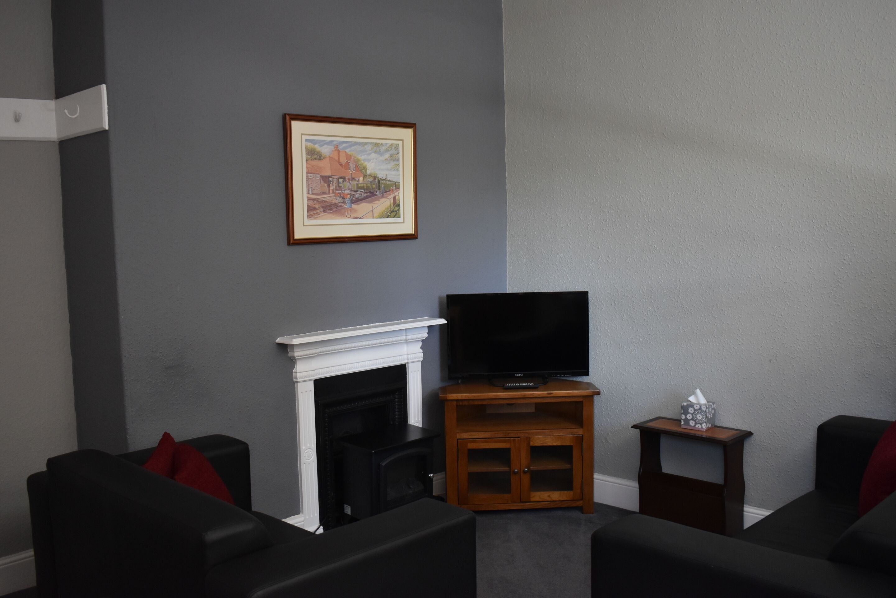 A living room with a fireplace, a television on a wooden stand, and two black sofas with red cushions.