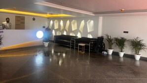 A reception area with a reception desk, a black sofa, a small table, and potted plants. - Hotel Grey Sky  (New Delhi)