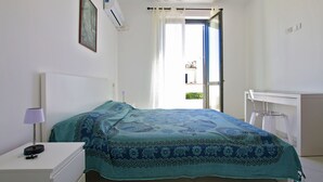 Een slaapkamer met een bed, een bureau, een airconditioner en een raam met gordijnen.