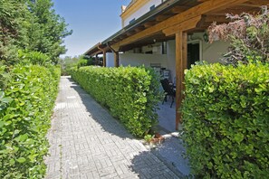 A paved pathway flanked by neatly trimmed hedges leading to a building with a wooden pergola. - Villa Enjoy - 3 bedrooms, close to the beach, in complex with pool available (Campofelice di Roccella)
