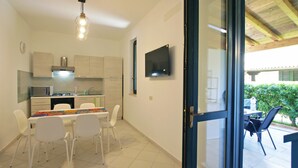 Een moderne keuken met witte kasten, een magnetron en een gasfornuis. Er is een zithoek met een tafel en stoelen, en een aan de muur bevestigde televisie.