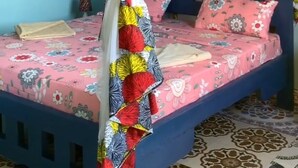 A single bed with a blue headboard, a canopy with a colorful quilt, and a floral-patterned bedspread. - COCCOBELLO ZANZIBAR (Kendwa)