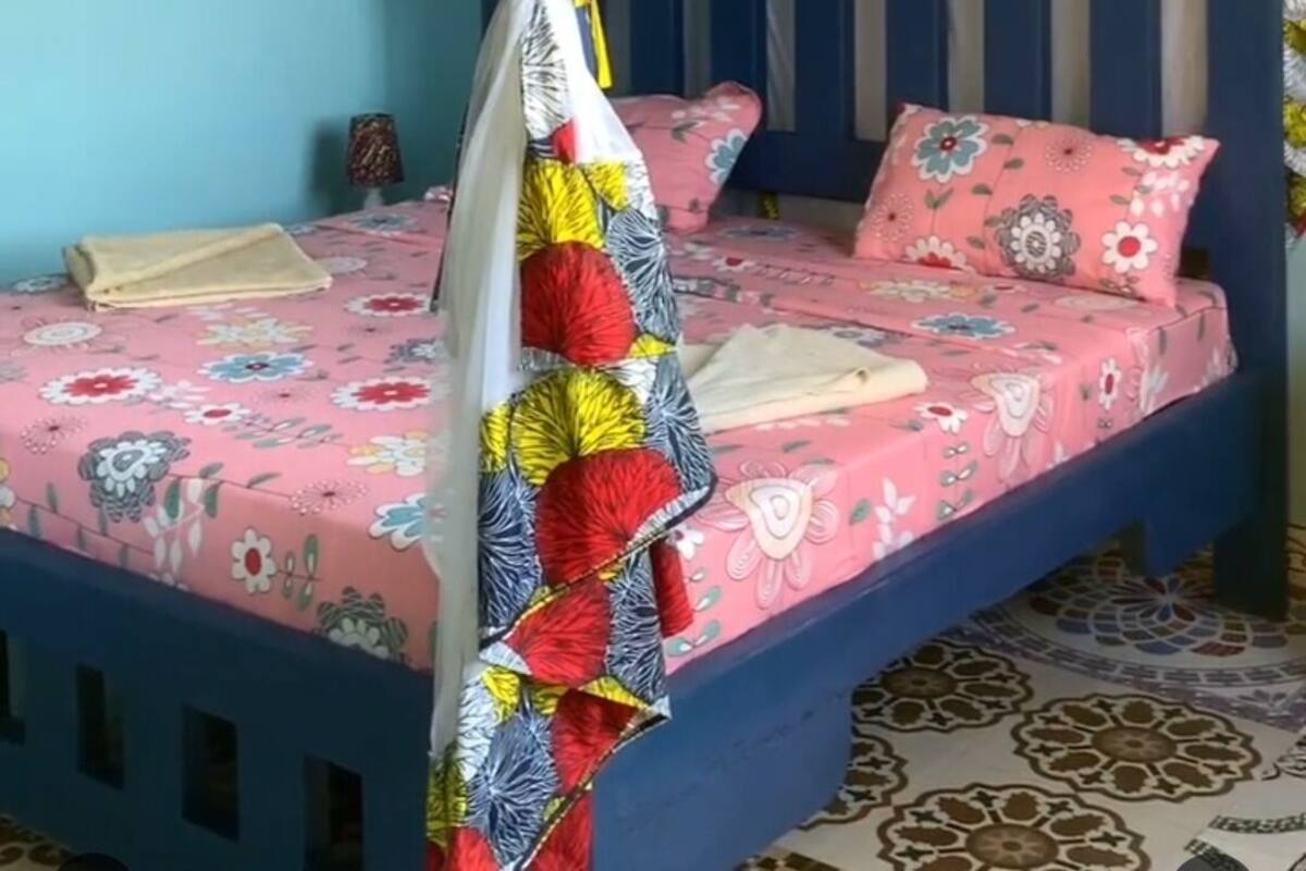 A single bed with a blue headboard, a canopy with a colorful quilt, and a floral-patterned bedspread.