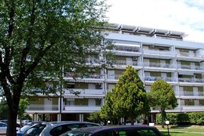 Un immeuble à plusieurs étages doté de balcons, avec des voitures garées et des arbres.