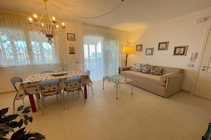 A dining area with a table and chairs, a sofa, a small table, and a chandelier.