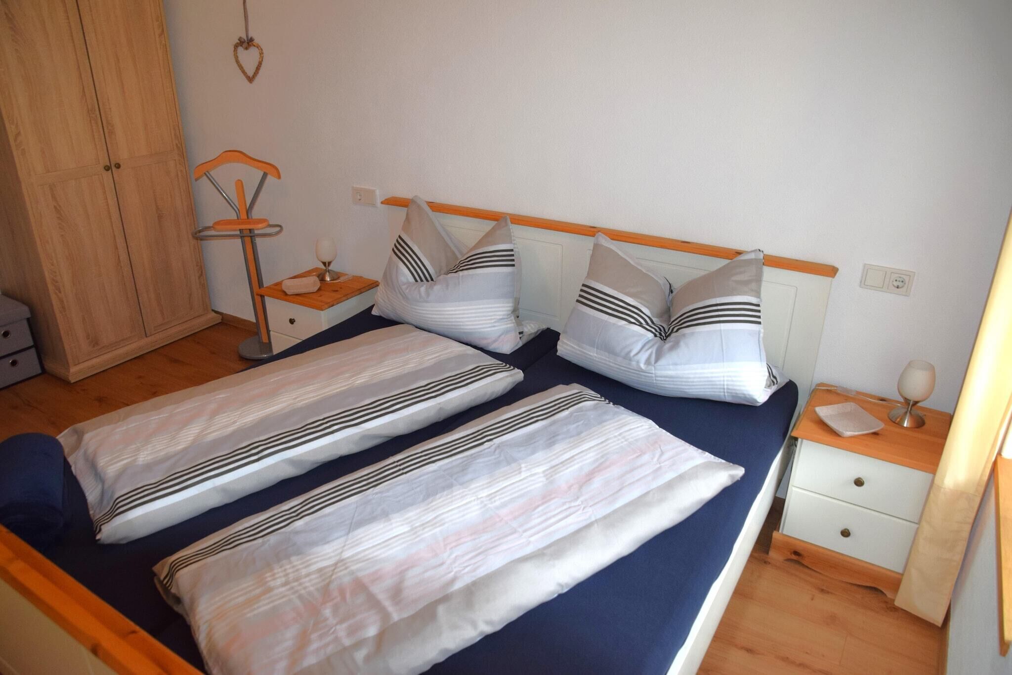 A twin room with two single beds, a wooden wardrobe, a bedside table with a lamp, and a small shelf.