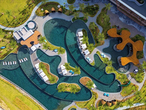 Eine Vogelperspektive eines Resorts mit mehreren Schwimmbecken, Liegebereichen und angelegten Gärten.