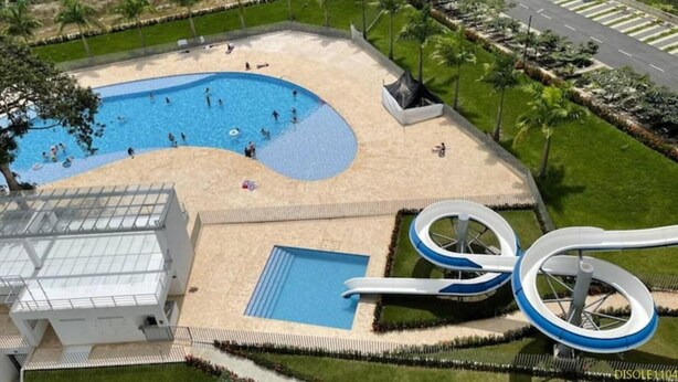 A swimming pool with a slide and a small adjacent pool, surrounded by a landscaped area with palm trees and a road in the background. - ¡Te va a Encantar! Disole 1104 (Santa Fé de Antioquia)